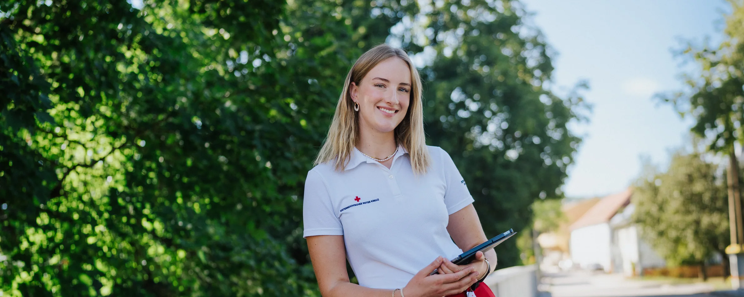 Eine Fundraiserin steht lächelnd an einem Geländer, im Hintergrund ein Dorf